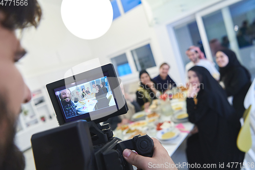 Image of Professional videograph recording video while Muslim family having iftar together during Ramadan