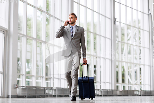Image of businessman with travel bag calling on smartphone