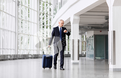 Image of senior businessman walking with travel bag