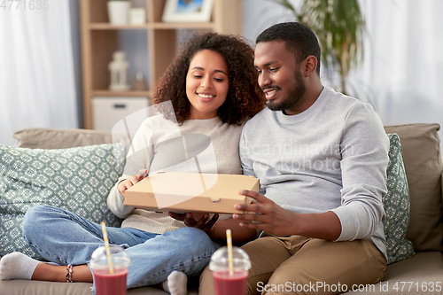 Image of happy african american couple eating pizza at home