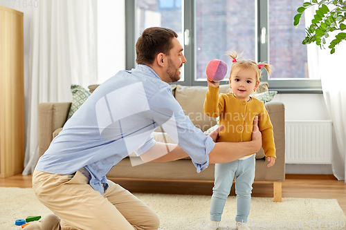 Image of father and baby daughter playing with ball at home