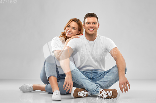 Image of happy couple in white t-shirts sitting on floor