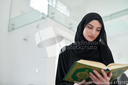 Image of Portrait of young muslim woman reading Quran in modern home