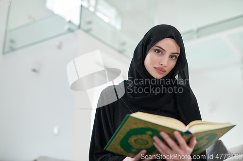 Image of Portrait of young muslim woman reading Quran in modern home