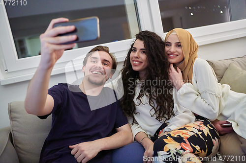 Image of Young happy, muslims taking selfie in house