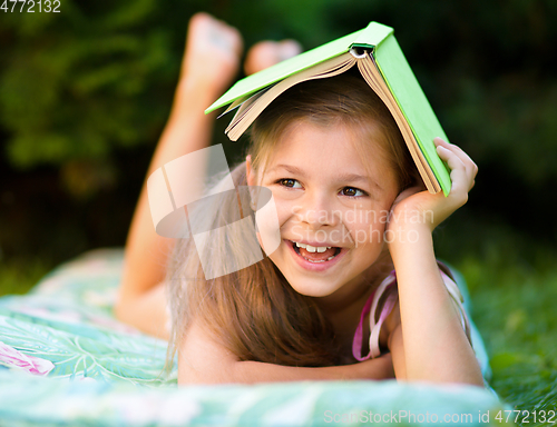 Image of Little girl is hiding under book outdoors