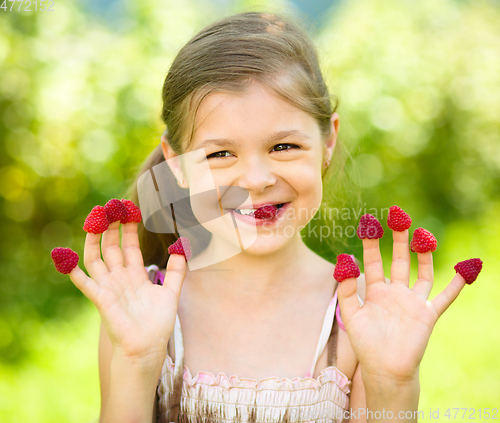 Image of Young girl is holding raspberries on her fingers