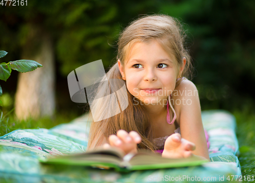 Image of Little girl is reading a book outdoors