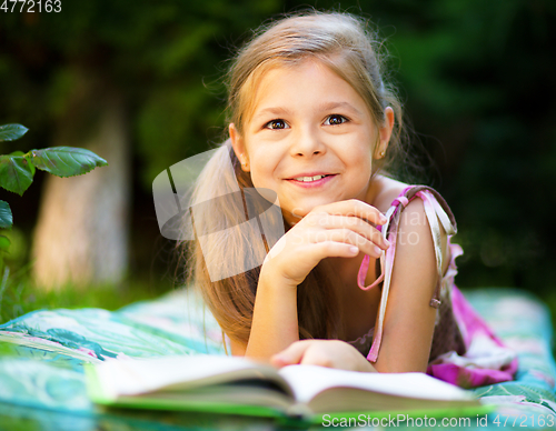Image of Little girl is reading a book outdoors