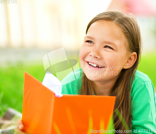 Image of Little girl is reading a book outdoors