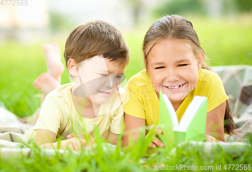 Image of Little girl and boy are reading book outdoors