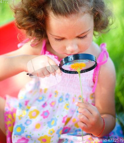 Image of Young girl is looking at flower through magnifier
