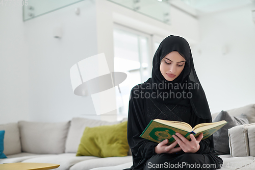 Image of Portrait of young muslim woman reading Quran in modern home