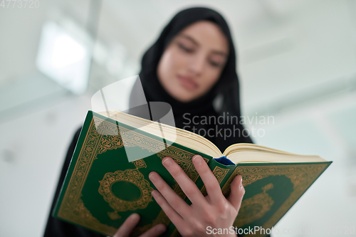 Image of Portrait of young muslim woman reading Quran in modern home