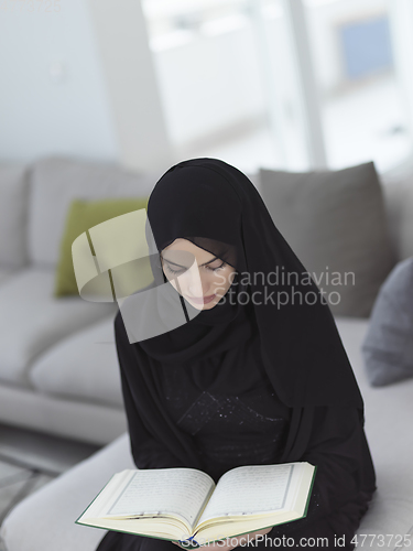 Image of Portrait of young muslim woman reading Quran in modern home