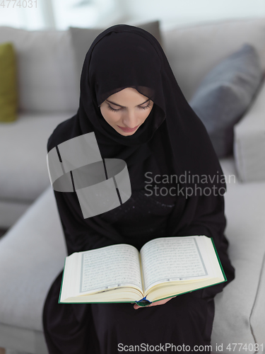 Image of Portrait of young muslim woman reading Quran in modern home