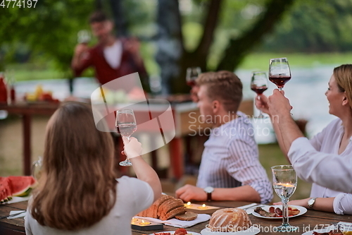 Image of friends toasting red wine glass while having picnic french dinner party outdoor