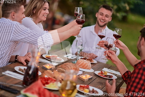 Image of friends toasting red wine glass while having picnic french dinner party outdoor