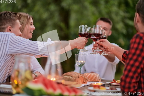 Image of friends toasting red wine glass while having picnic french dinner party outdoor