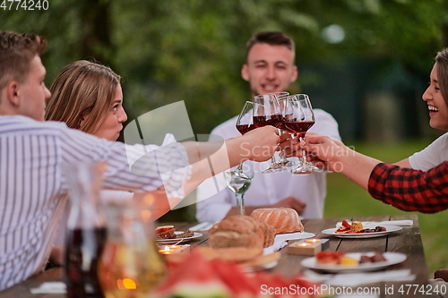 Image of friends toasting red wine glass while having picnic french dinner party outdoor