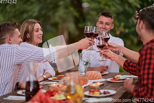 Image of friends toasting red wine glass while having picnic french dinner party outdoor
