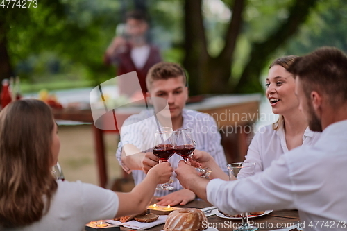 Image of friends toasting red wine glass while having picnic french dinner party outdoor