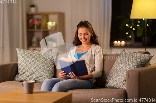 Image of young woman reading book at home in evening