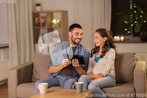 Image of happy couple using tablet pc at home in evening