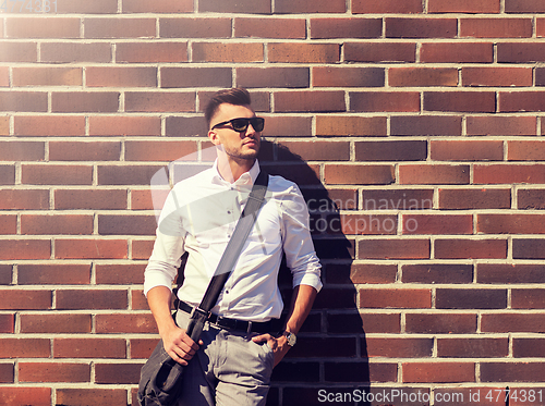 Image of young man in sunglasses with bag over brickwall