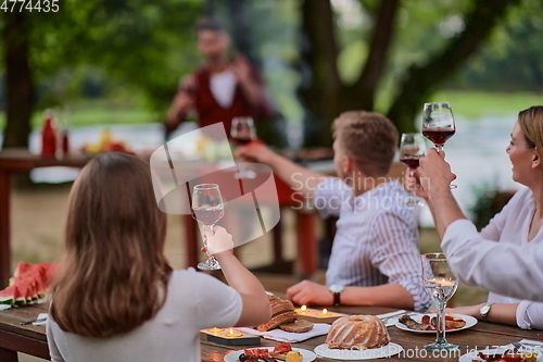 Image of friends toasting red wine glass while having picnic french dinner party outdoor