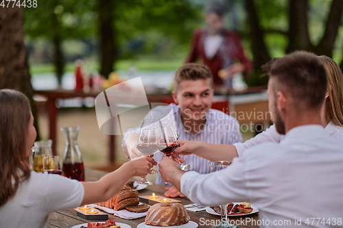 Image of friends toasting red wine glass while having picnic french dinner party outdoor