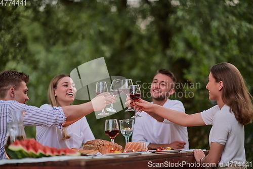 Image of friends toasting red wine glass while having picnic french dinner party outdoor