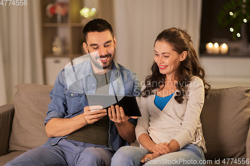 Image of happy couple using tablet pc at home in evening