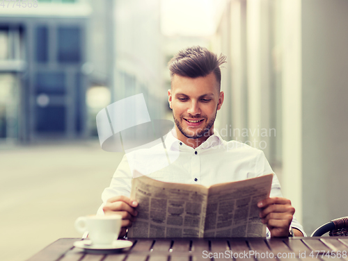 Image of smiling man reading newspaper at city street cafe