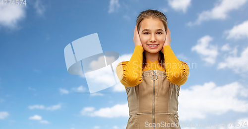 Image of smiling teenage girl closing ears over sky