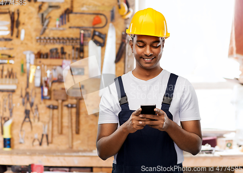 Image of happy indian or builder in helmet using smartphone