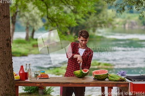 Image of man cutting juicy watermelon during outdoor french dinner party