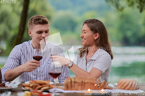 Image of couple toasting red wine glass while having picnic french dinner party outdoor