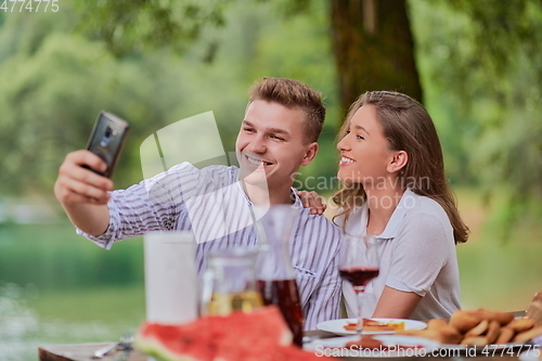 Image of couple taking selfie while having picnic french dinner party outdoor