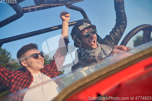 Image of two young happy excited men enjoying beautiful sunny day while driving a off road buggy car