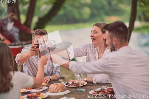 Image of friends toasting red wine glass while having picnic french dinner party