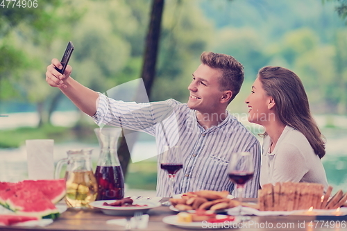 Image of couple taking selfie while having picnic french dinner party outdoor