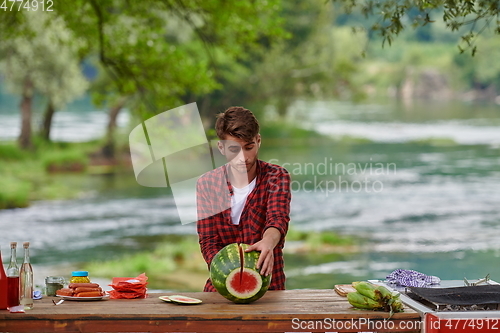 Image of man cutting juicy watermelon during outdoor french dinner party