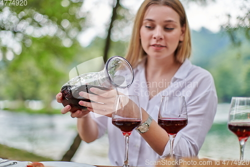 Image of woman pouring red wine into glasses