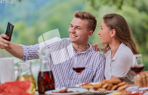 Image of couple taking selfie while having picnic french dinner party outdoor