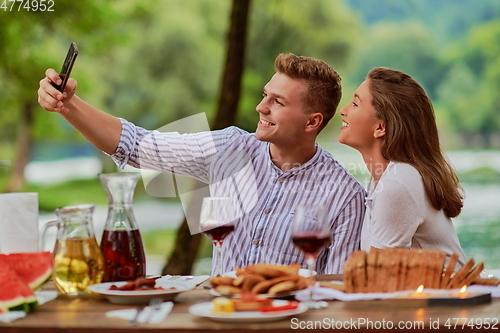 Image of couple taking selfie while having picnic french dinner party outdoor