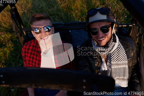 Image of two young happy excited men enjoying beautiful sunny day while driving a off road buggy car
