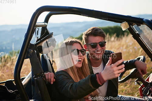 Image of couple enjoying beautiful sunny day taking selfie picture while driving a off road buggy