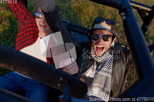 Image of two young happy excited men enjoying beautiful sunny day while driving a off road buggy car