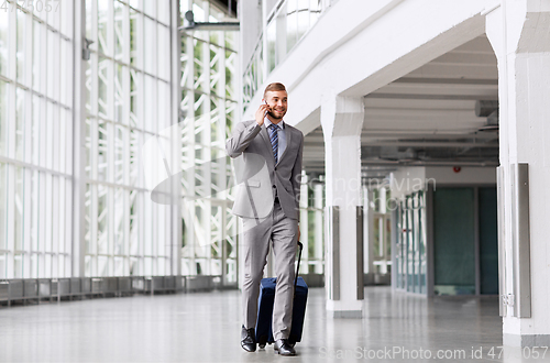 Image of businessman with travel bag calling on smartphone